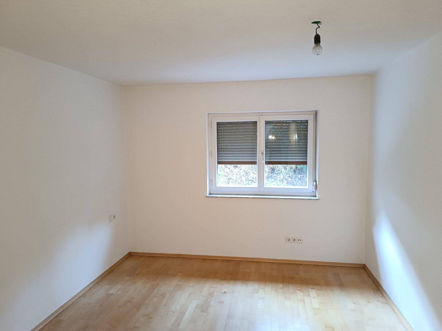 Schlafzimmer mit hellem Holzboden und einem Fenster, das mit einem Rollladen ausgestattet ist.