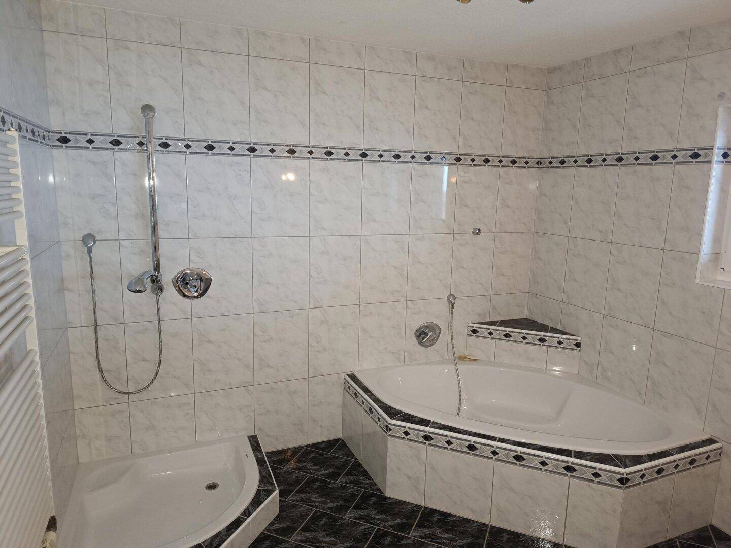 Badezimmer mit Eckbadewanne, separater Dusche und hellen Fliesen mit dekorativer Bordüre.