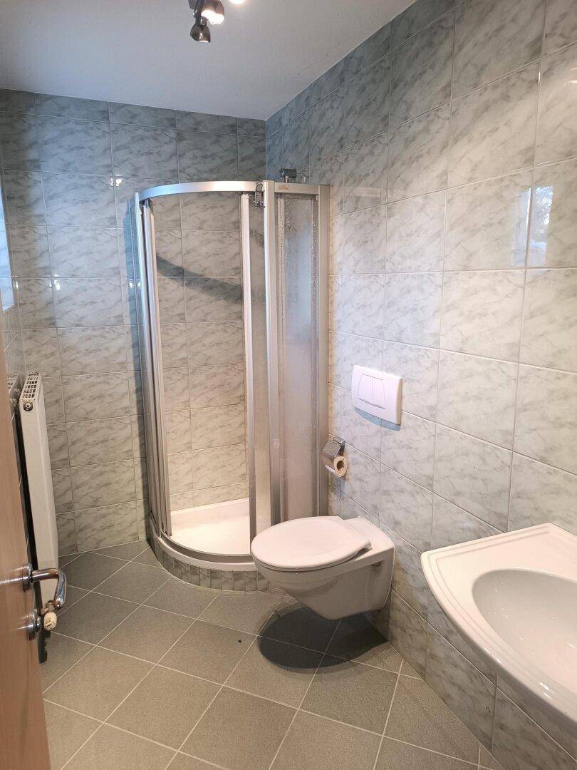 Badezimmer mit Duschkabine, WC und Waschbecken, ausgestattet mit hellgrauen Fliesen.