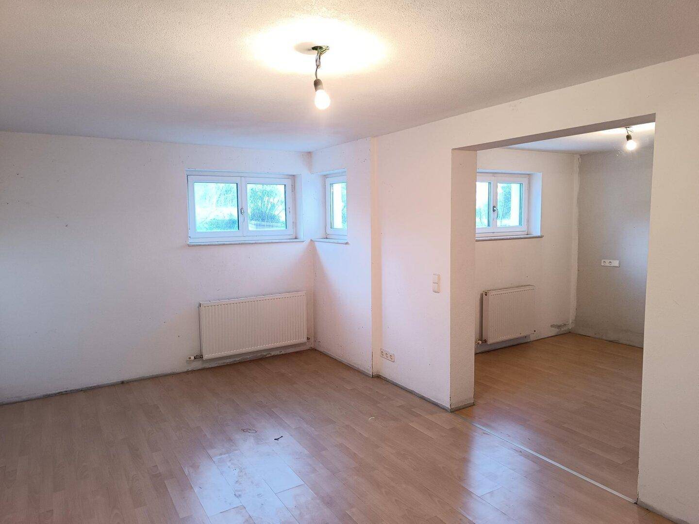 Geräumiger Wohnbereich mit Holzboden, mehreren Fenstern und Heizkörpern, ideal für Gestaltung.
