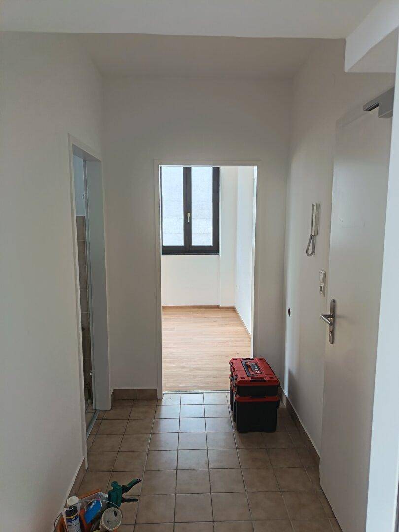 Heller Flur mit Fliesenboden und Blick in ein weiteres Zimmer, gut beleuchtet.