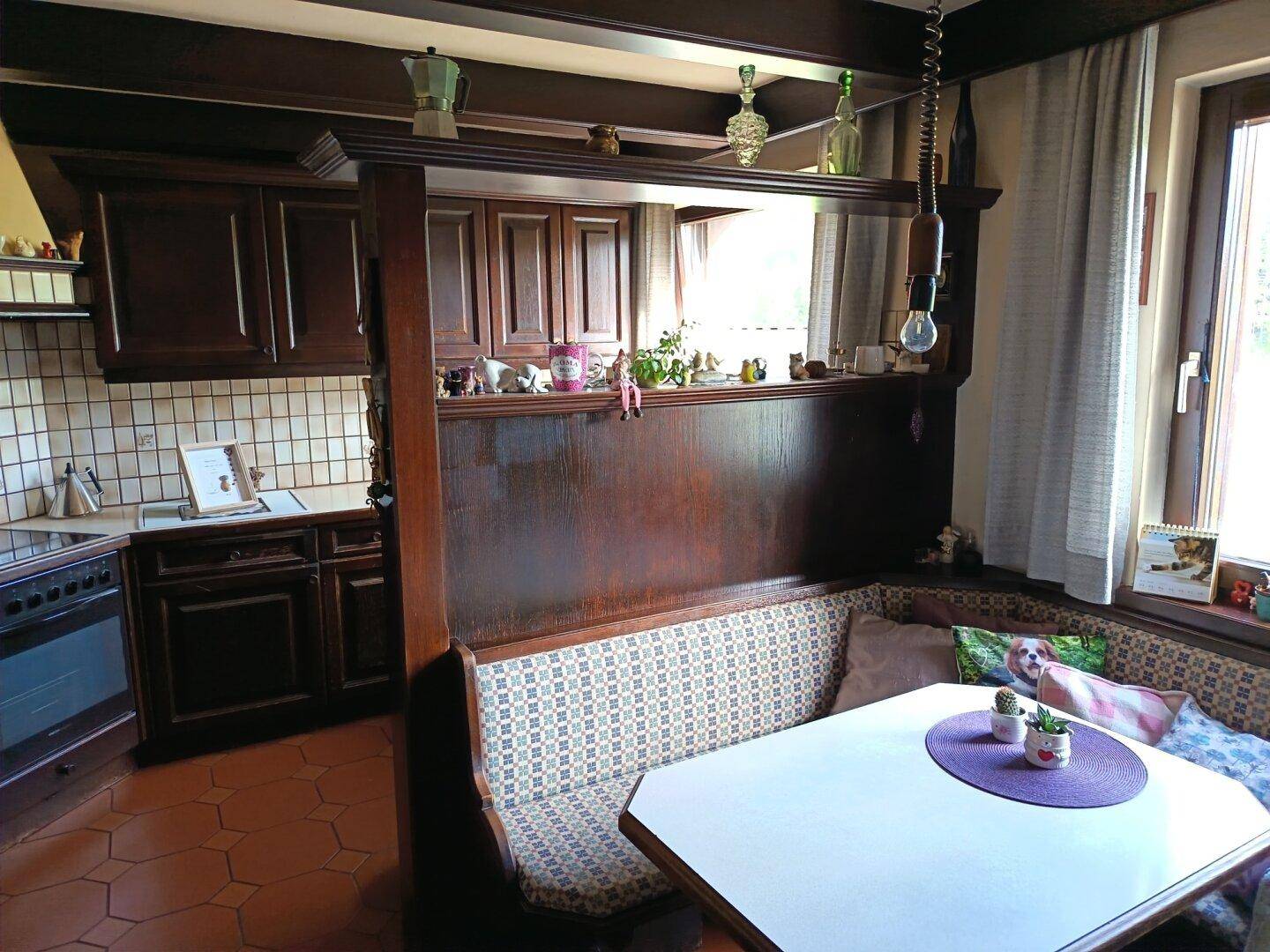 Traditionelle Holzküche mit Essbereich, Fliesenboden und Blick nach draußen durch das Fenster.