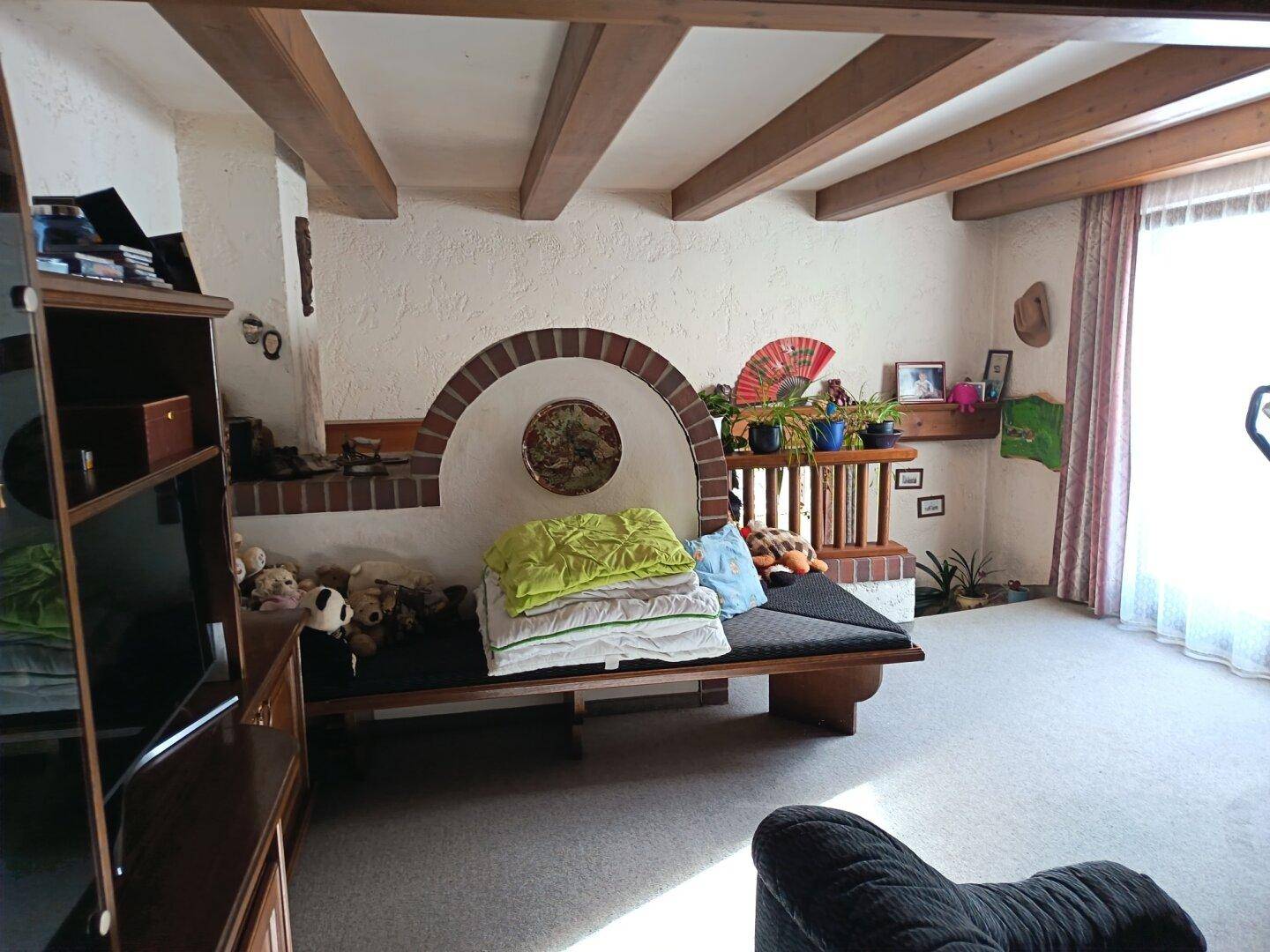 Helles Wohnzimmer mit Teppichboden, Holzbalken und einem gemauerten Kamin mit integrierter Sitzbank.