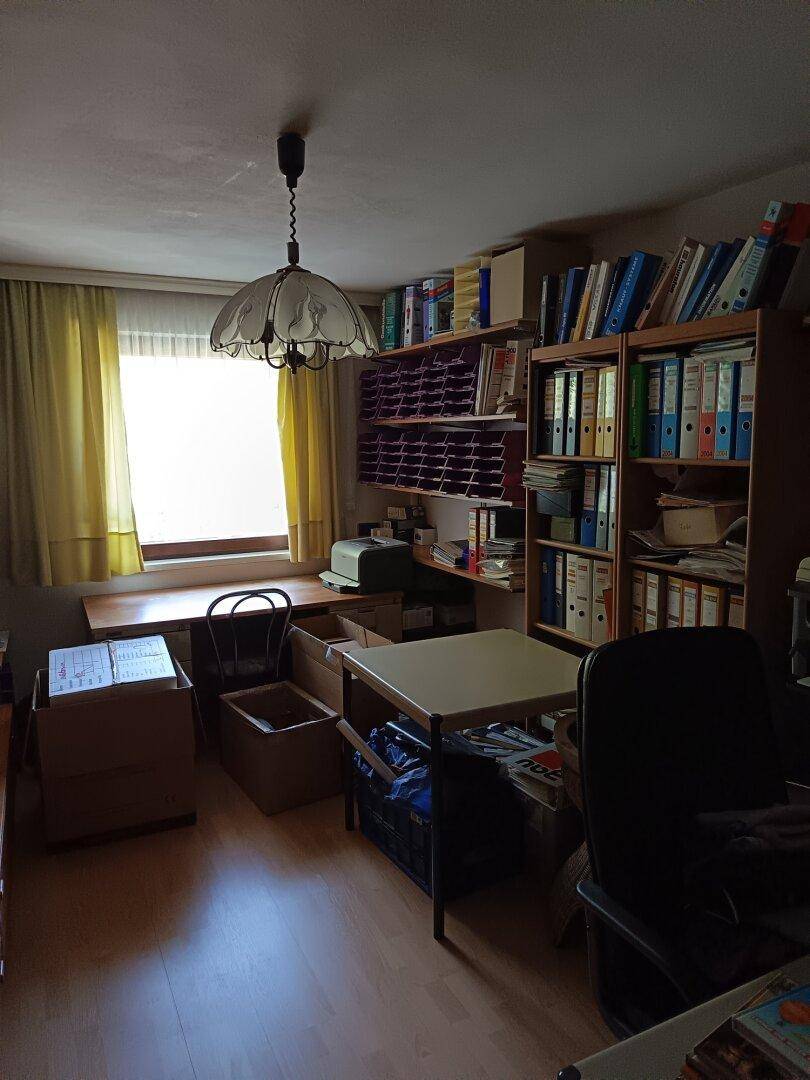 Funktionales Arbeitszimmer mit Holzfußboden, Bücherregalen und einem Fenster, das Tageslicht hereinlässt.