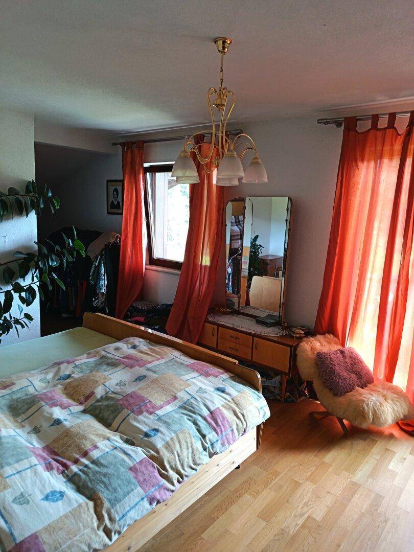 Schlafzimmer mit Holzbett, Laminatboden und einem Fenster mit orangefarbenen Vorhängen.