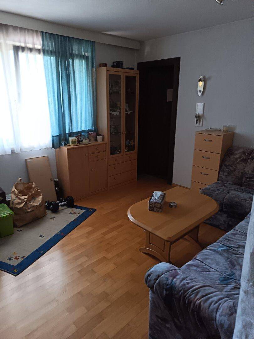 Helles Wohnzimmer mit Holzfußboden, großem Fenster und gemütlichem Sofa, eingerichtet mit Holzmöbeln.