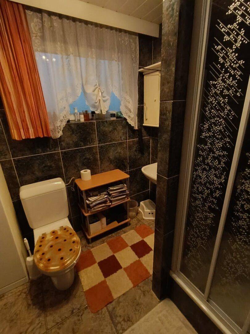 Kleines Badezimmer mit Toilette, Waschbecken und Duschkabine, ausgestattet mit dunklen Fliesen.
