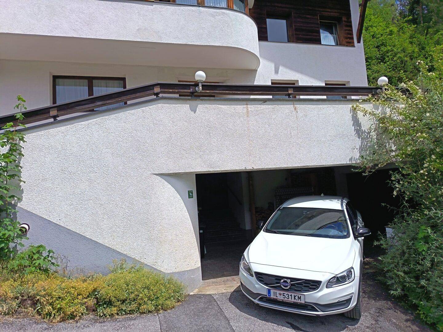 Einfahrt zur Tiefgarage mit einem weißen Auto und einer weißen Hausfassade im Vordergrund.