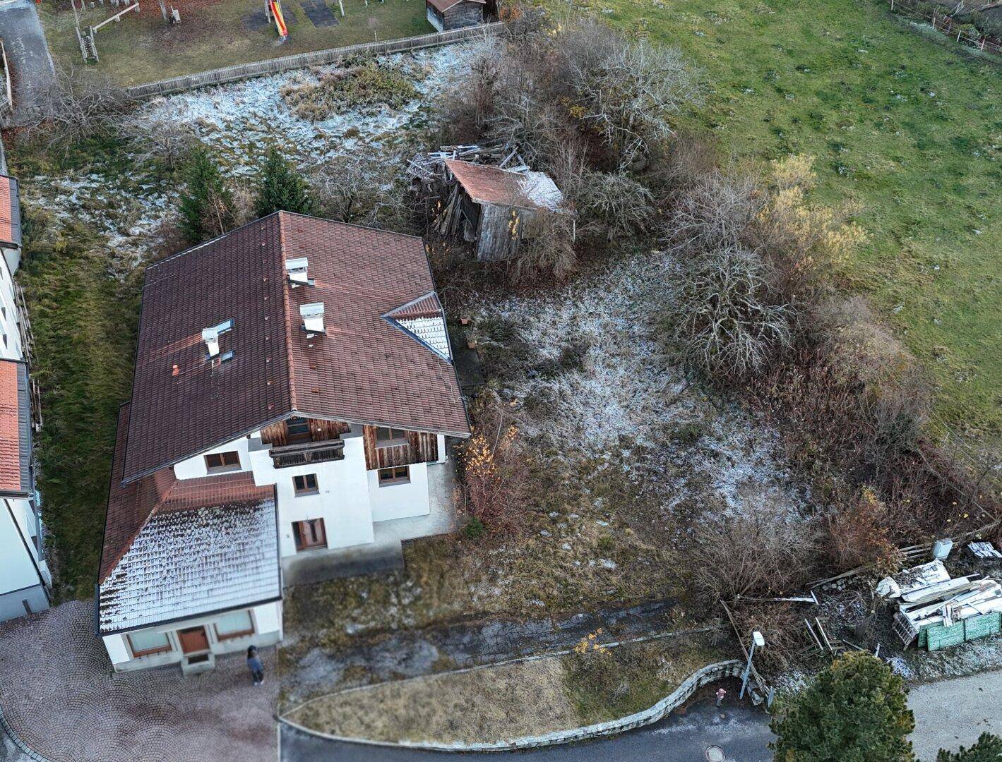 Detaillierte Luftaufnahme eines Wohnhauses mit braunem Dach und einem alten Schuppen auf dem Grundstück.