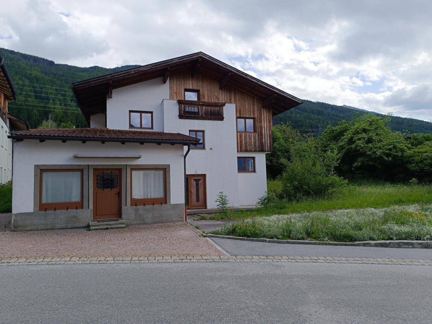 Vorderansicht des Wohnhauses mit weißer Fassade, Holzelementen und einem kleinen Anbau an der Straße.