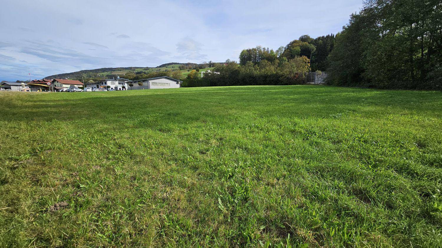 Großes, offenes Wiesengrundstück mit Blick auf die umliegenden Hügel und einige Gebäude in der Ferne.