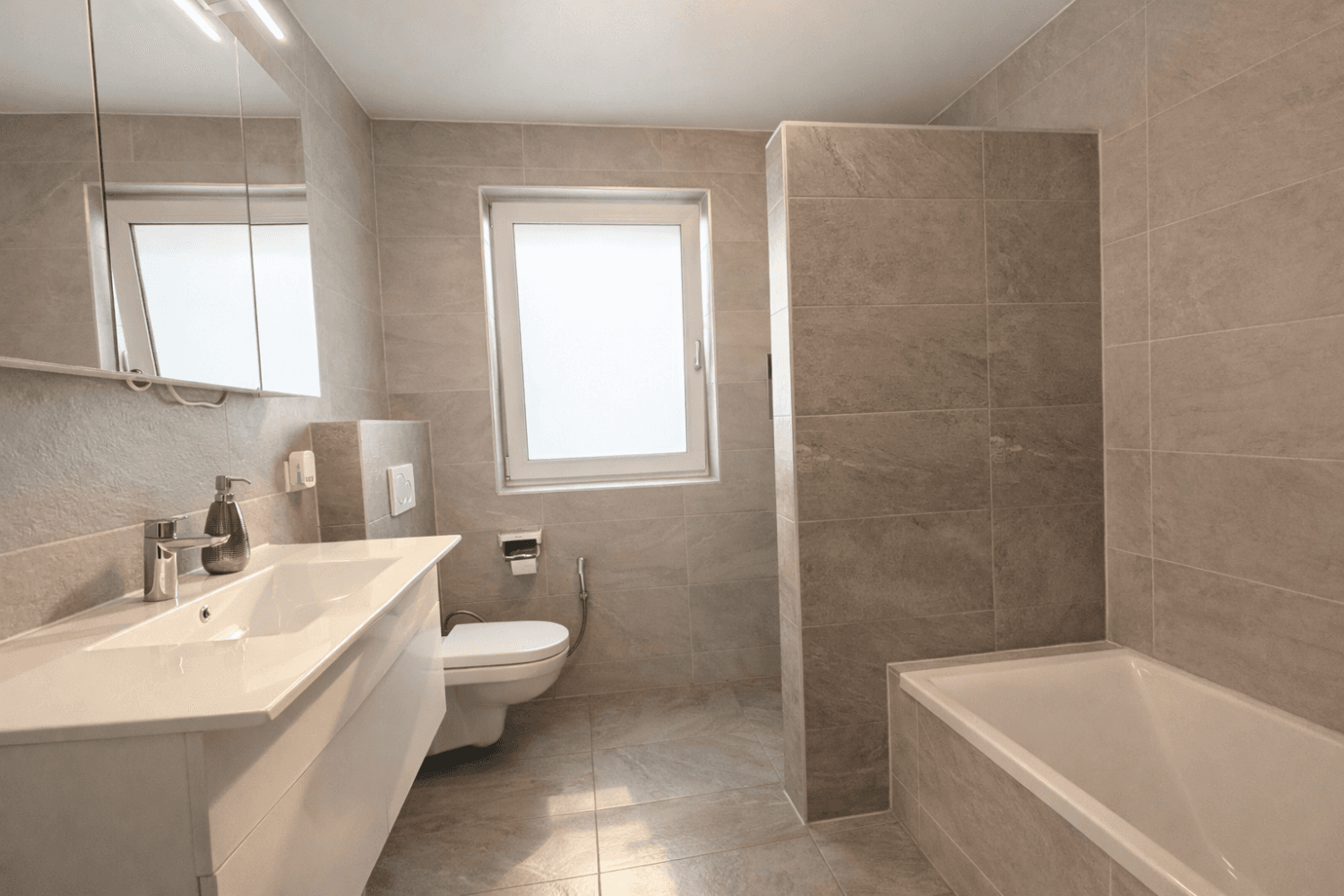 Modernes Badezimmer mit grauen Fliesen, Badewanne, wandhängendem WC und Einzelwaschbecken.