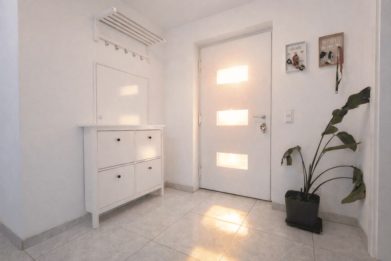 Freundlicher Eingangsbereich mit weißer Tür, Fliesenboden, Schuhschrank und Garderobe.