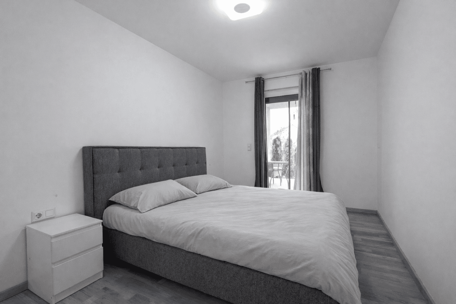 Schlafzimmer in Schwarz-Weiß mit Doppelbett und Zugang zu einem Balkon.