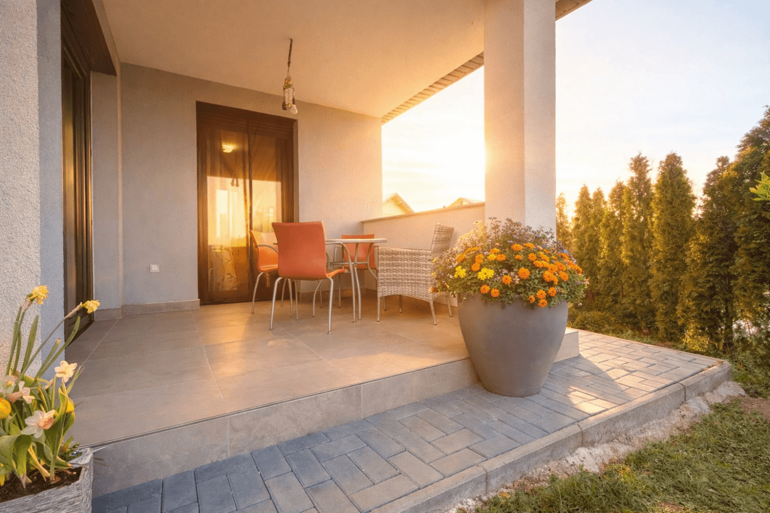 Überdachte Terrasse mit Gartenmöbeln und Pflanzen, beleuchtet von der Abendsonne.
