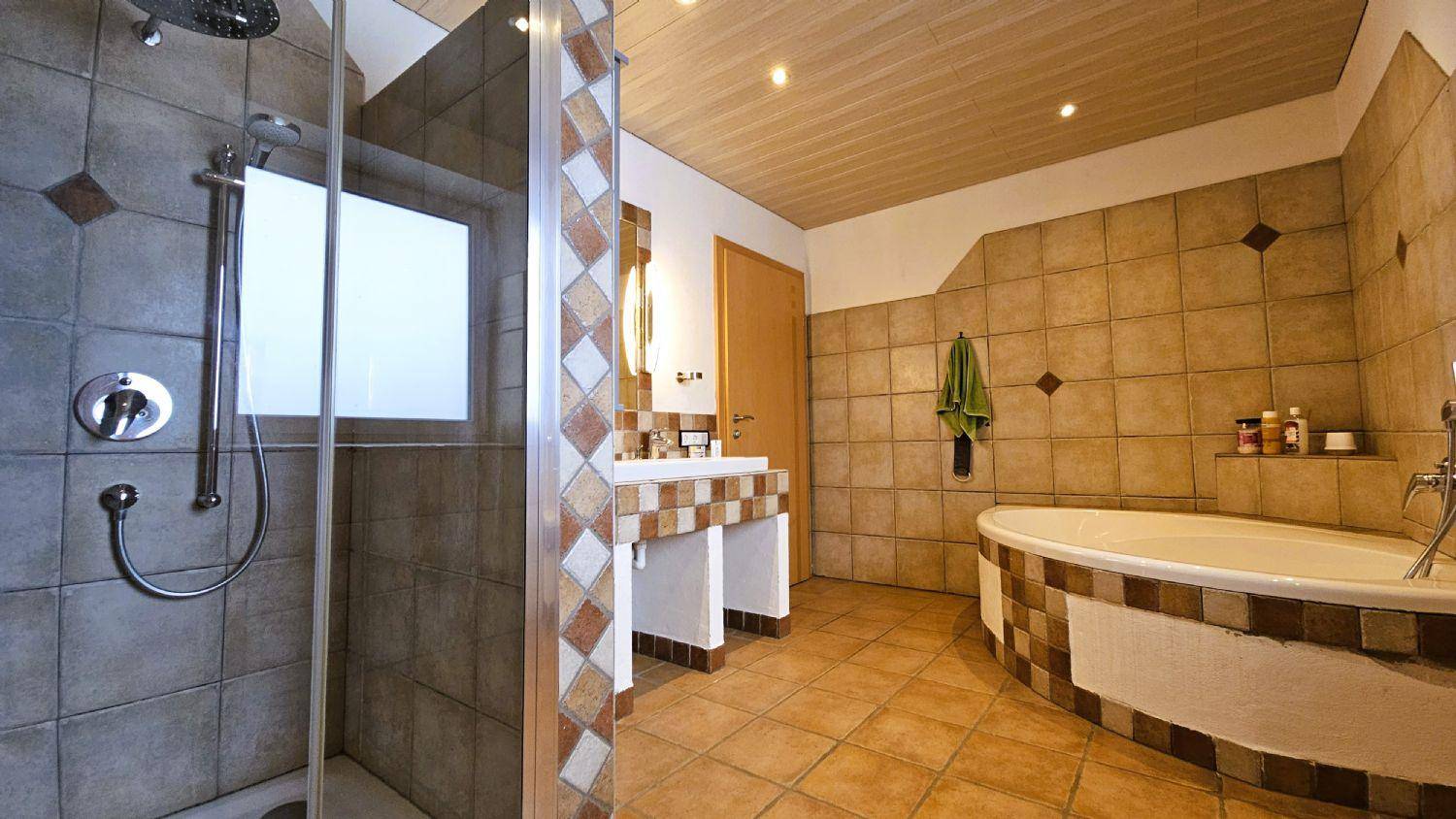 Geräumiges Badezimmer mit Badewanne, separater Dusche und gemusterten Fliesen.