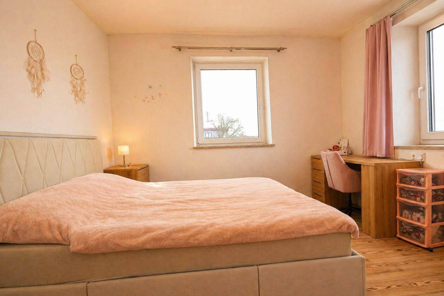 Helles Schlafzimmer mit Doppelbett, Schminktisch und Fenster mit Blick nach draußen.
