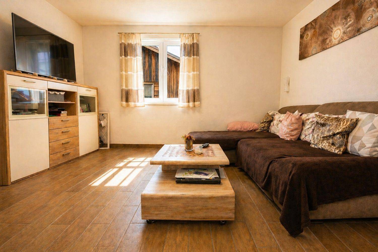 Gemütliches Wohnzimmer mit großem Sofa, Holzboden und Fernseher auf einem Sideboard.