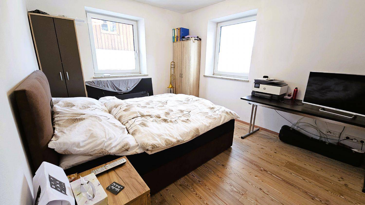 Schlafzimmer mit Doppelbett, Schreibtisch und zwei Fenstern für natürliches Licht.