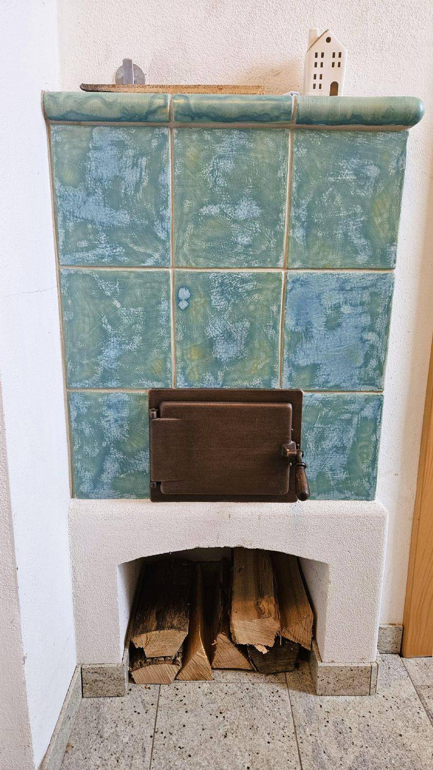Traditioneller Kachelofen mit blauen Fliesen und Holzscheiten darunter für gemütliche Wärme.