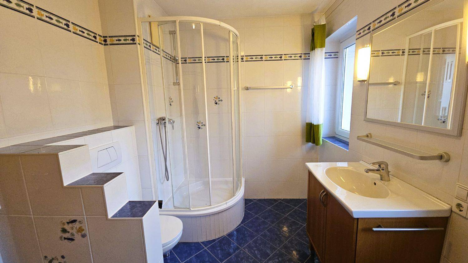 Helles Badezimmer mit Duschkabine, Waschtisch und blauen Bodenfliesen, ausgestattet mit Fenster.