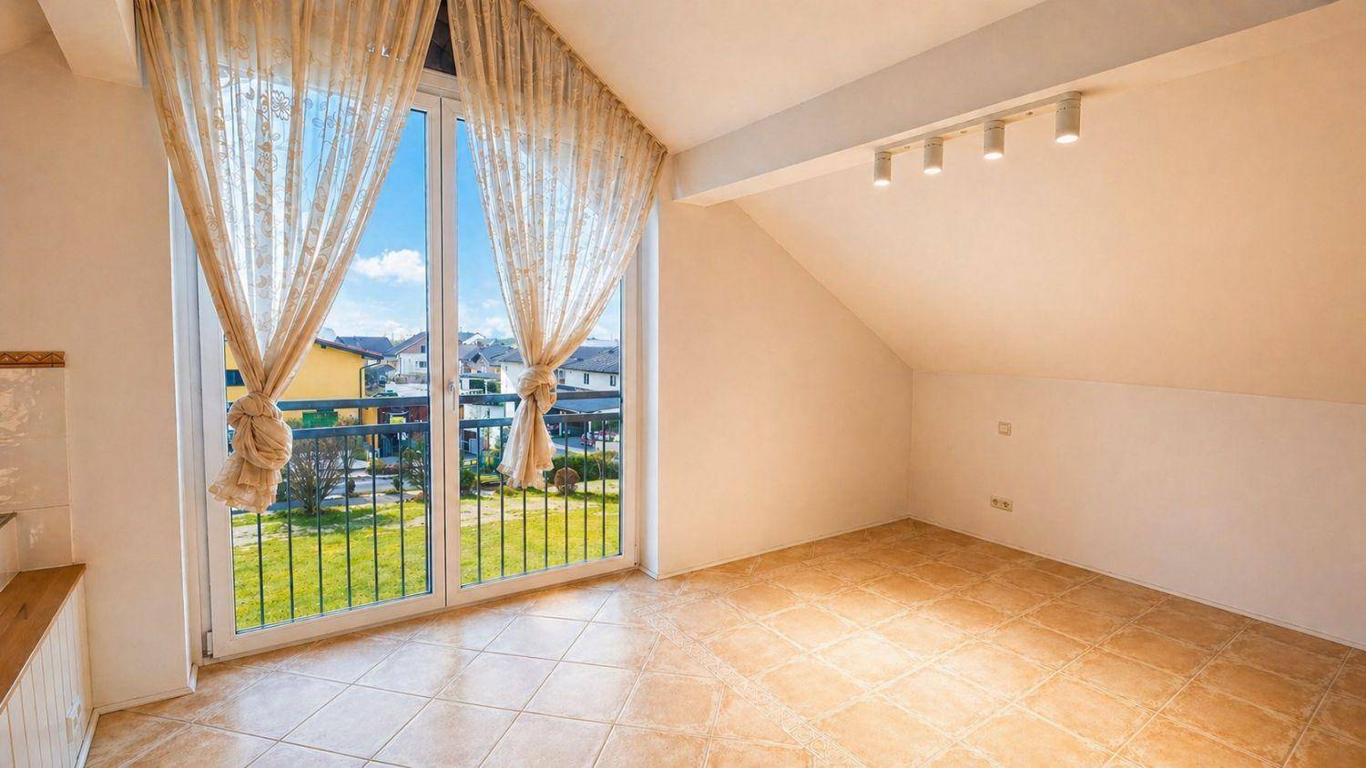 Heller, leerer Raum im Dachgeschoss mit Fliesenboden und Zugang zu einem französischen Balkon.