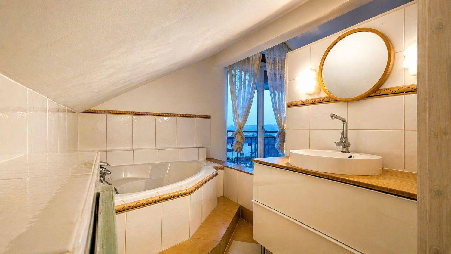Badezimmer im Dachgeschoss mit Eckbadewanne, modernem Waschbecken und Fenster mit Ausblick.
