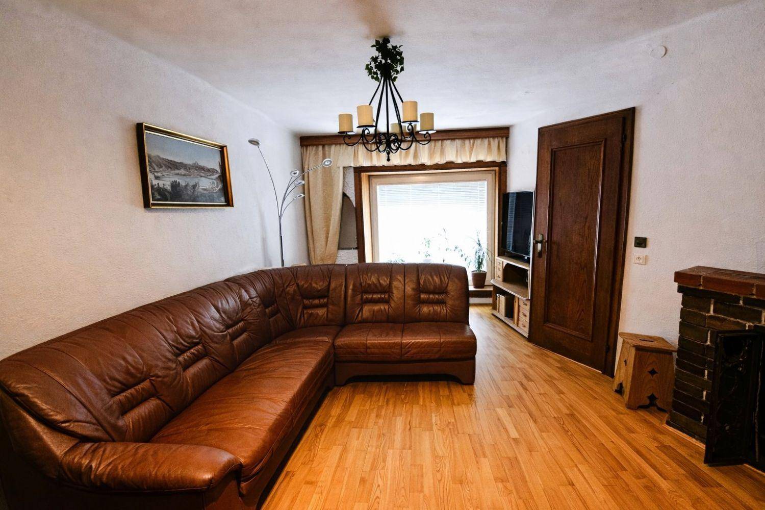 Geräumiges Wohnzimmer mit Ledersofa, Holzboden und gemauertem Kamin.