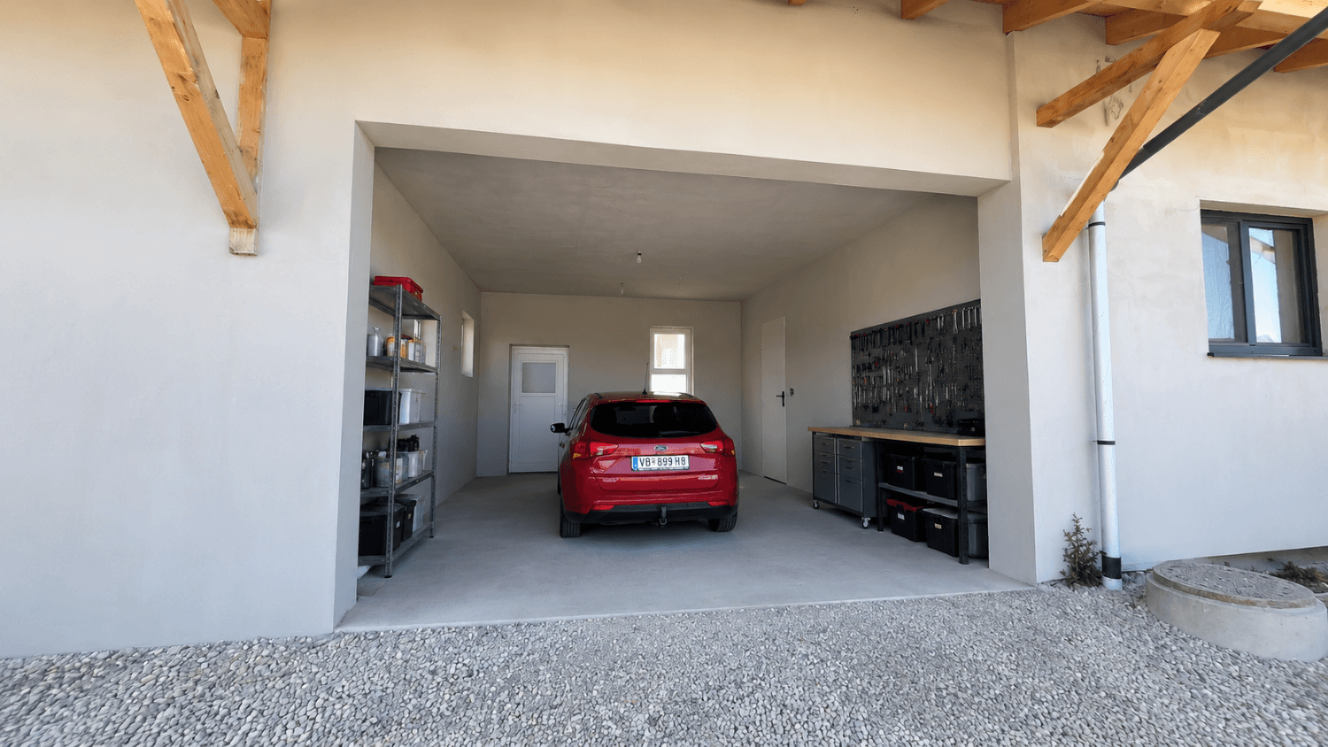 Überdachte Garage mit einem geparkten Auto, Regalen und Werkstattbereich, Teil eines Neubaus.