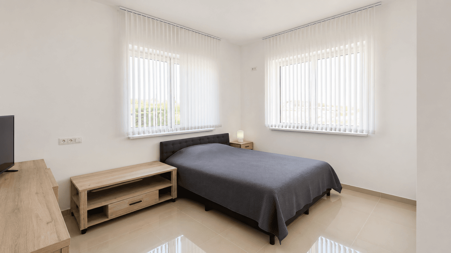 Helles Schlafzimmer mit Doppelbett, hellen Holzmöbeln und zwei großen Fenstern.