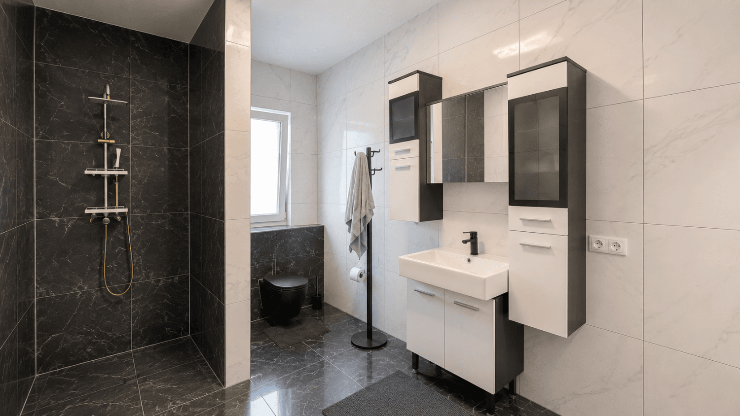 Modernes Badezimmer mit begehbarer Dusche, dunklen und hellen Fliesen sowie einem Fenster.