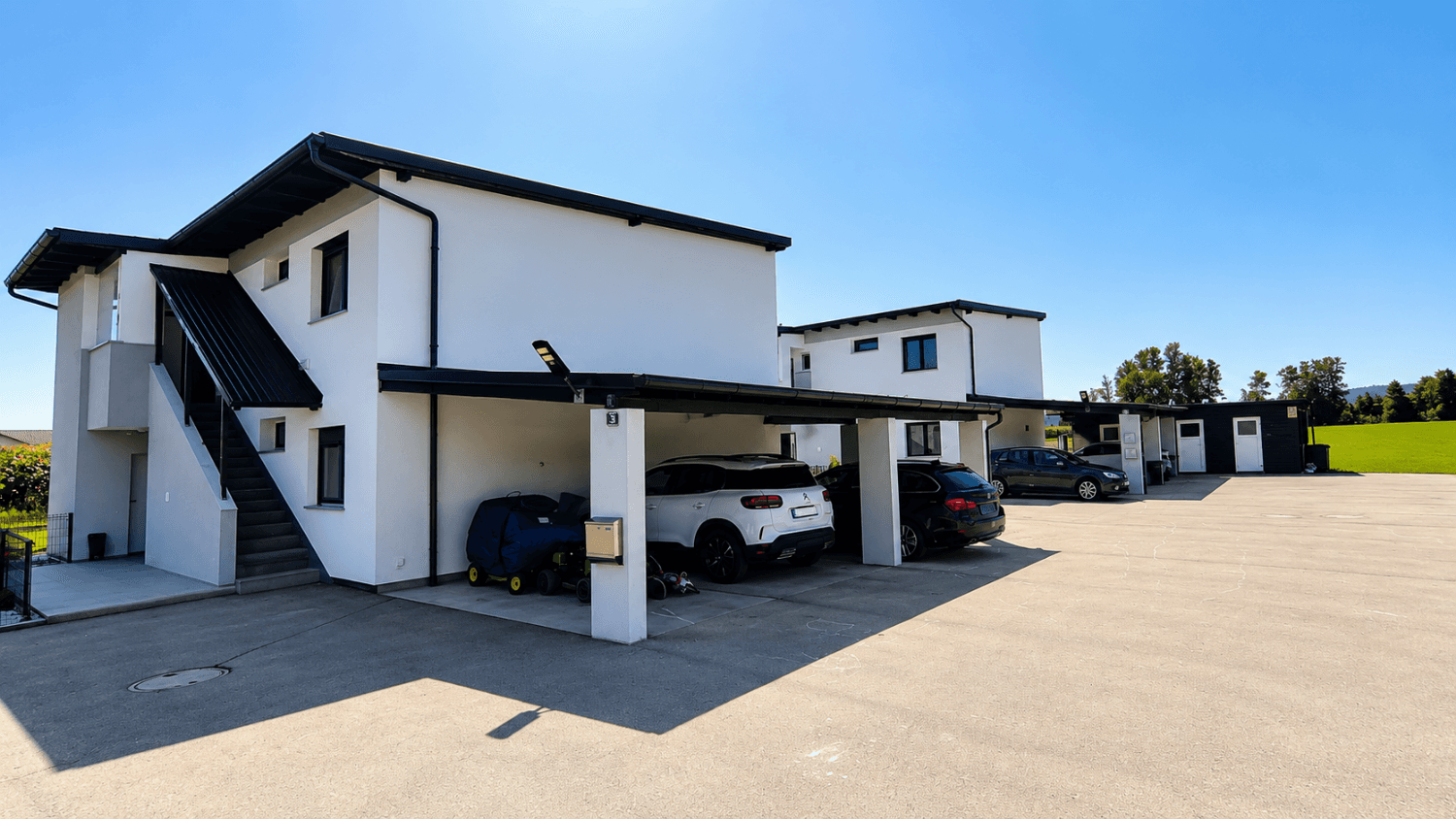 Moderne Reihenhäuser mit Carports und Flachdächern in sonniger Umgebung.