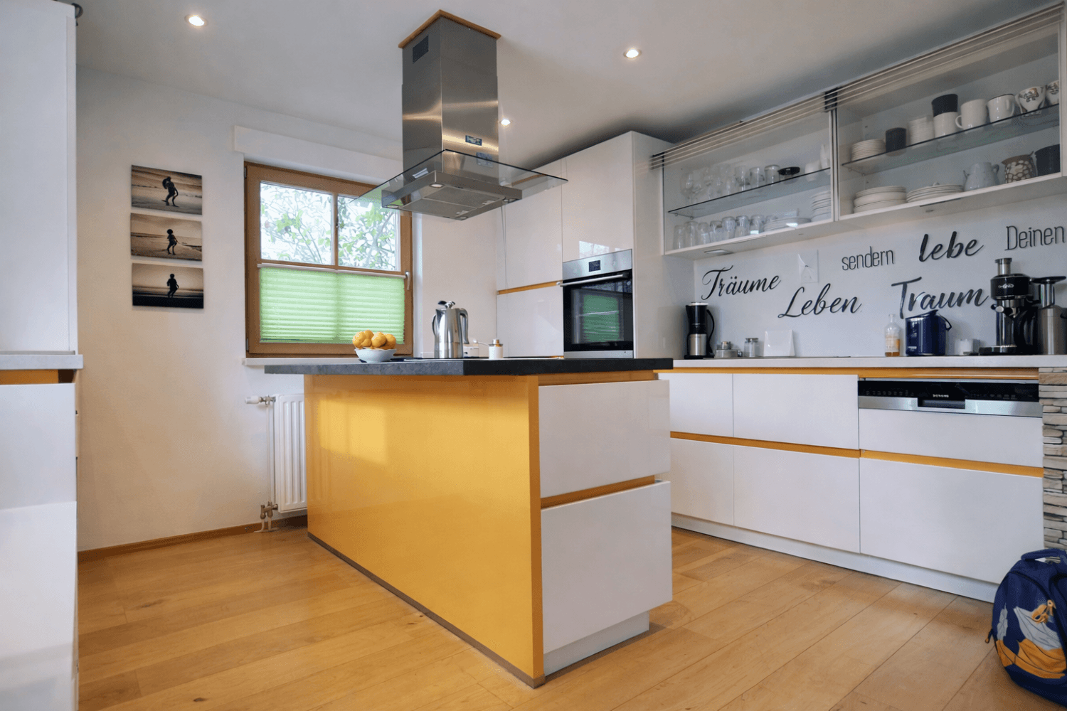 Moderne Küche mit weiß-gelben Fronten, Kücheninsel und hochwertigen Geräten.