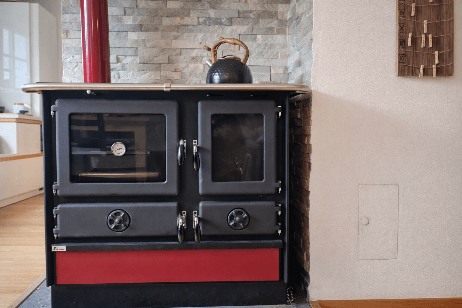 Traditioneller Holzofen mit rotem Sockel und Steinwand im Hintergrund.