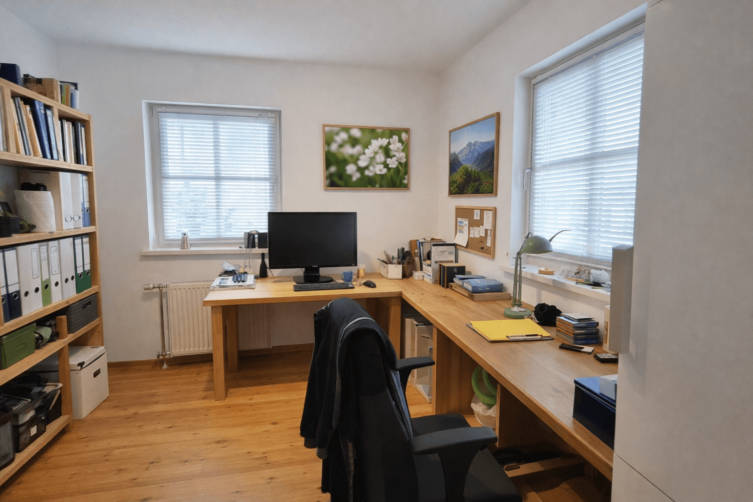 Geräumiges Büro mit Holztischen, Bücherregal und zwei großen Fenstern.