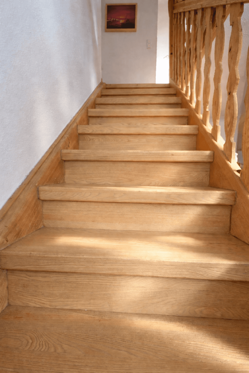 Helle Holztreppe mit Geländer, die in ein oberes Stockwerk führt.