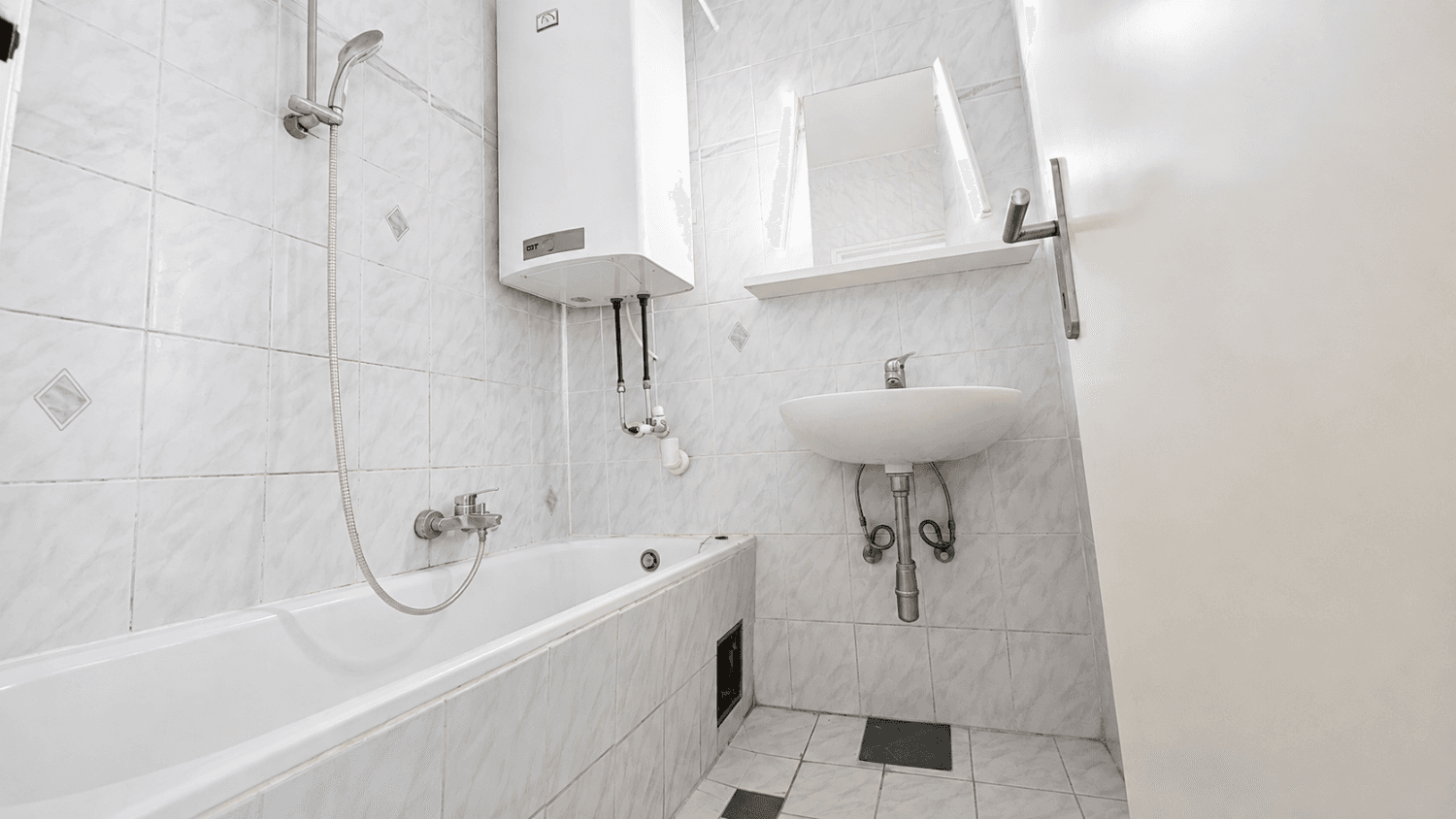 Gefliestes Badezimmer mit Badewanne, Waschbecken und Warmwasserboiler.