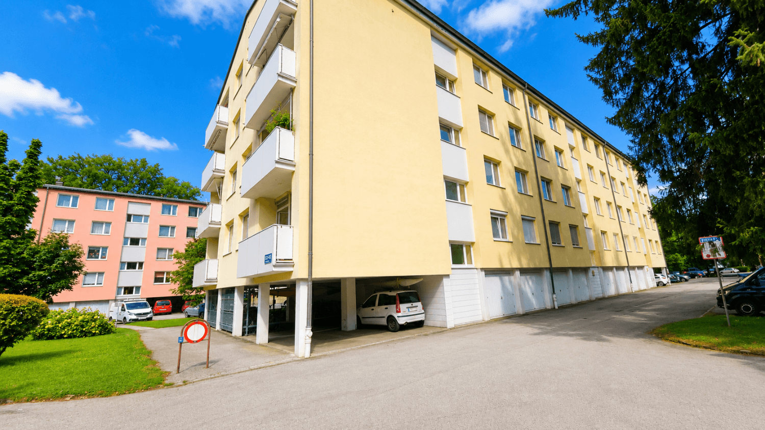 Mehrstöckiges Wohngebäude mit gelber Fassade, Balkonen und integrierten Garagen unter blauem Himmel.