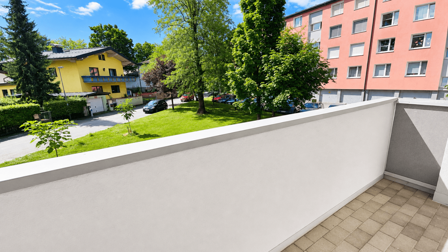 Heller Balkon mit Fliesenboden und weißer Brüstung, bietet Blick auf die grüne Umgebung.