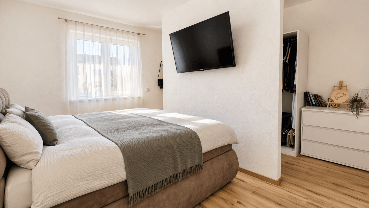 Gemütliches Schlafzimmer mit großem Bett, Wandfernseher und integriertem Kleiderschrankbereich.
