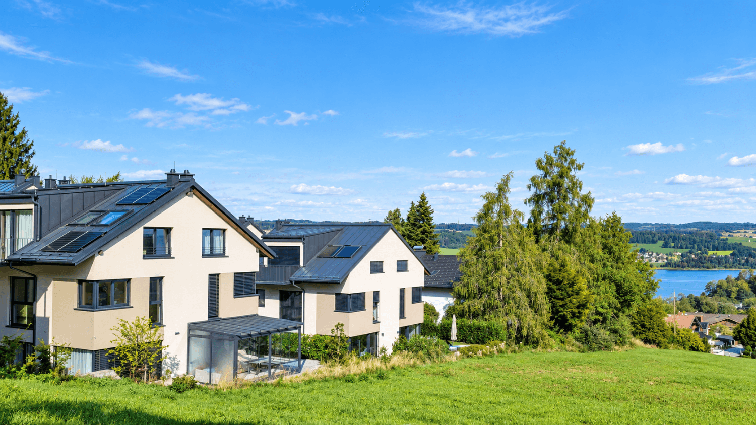 Mehrere moderne Häuser in einer grünen Landschaft mit Blick auf einen See.
