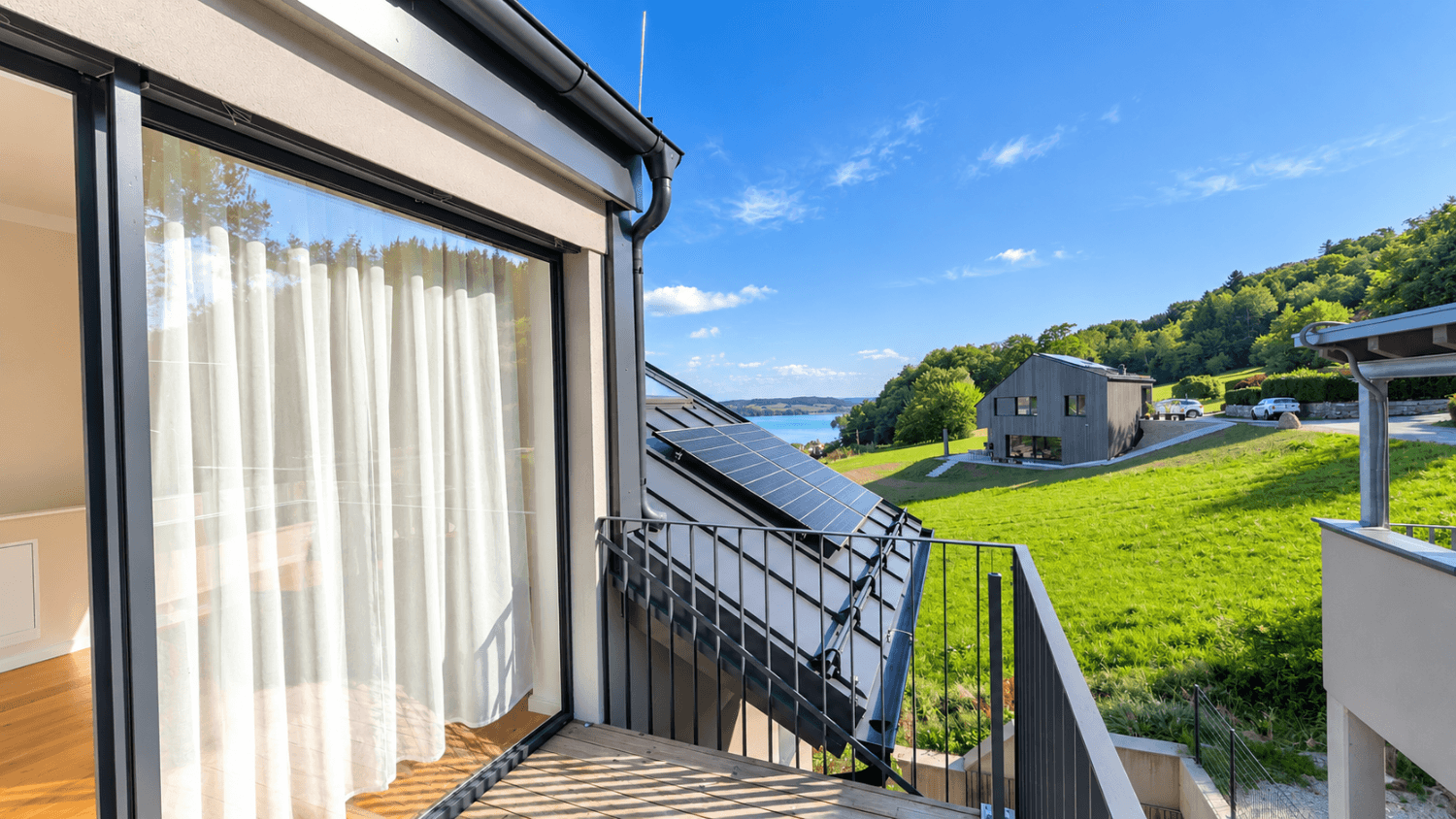 Balkon mit Metallgeländer und weitem Blick auf den See und die umliegende grüne Landschaft.