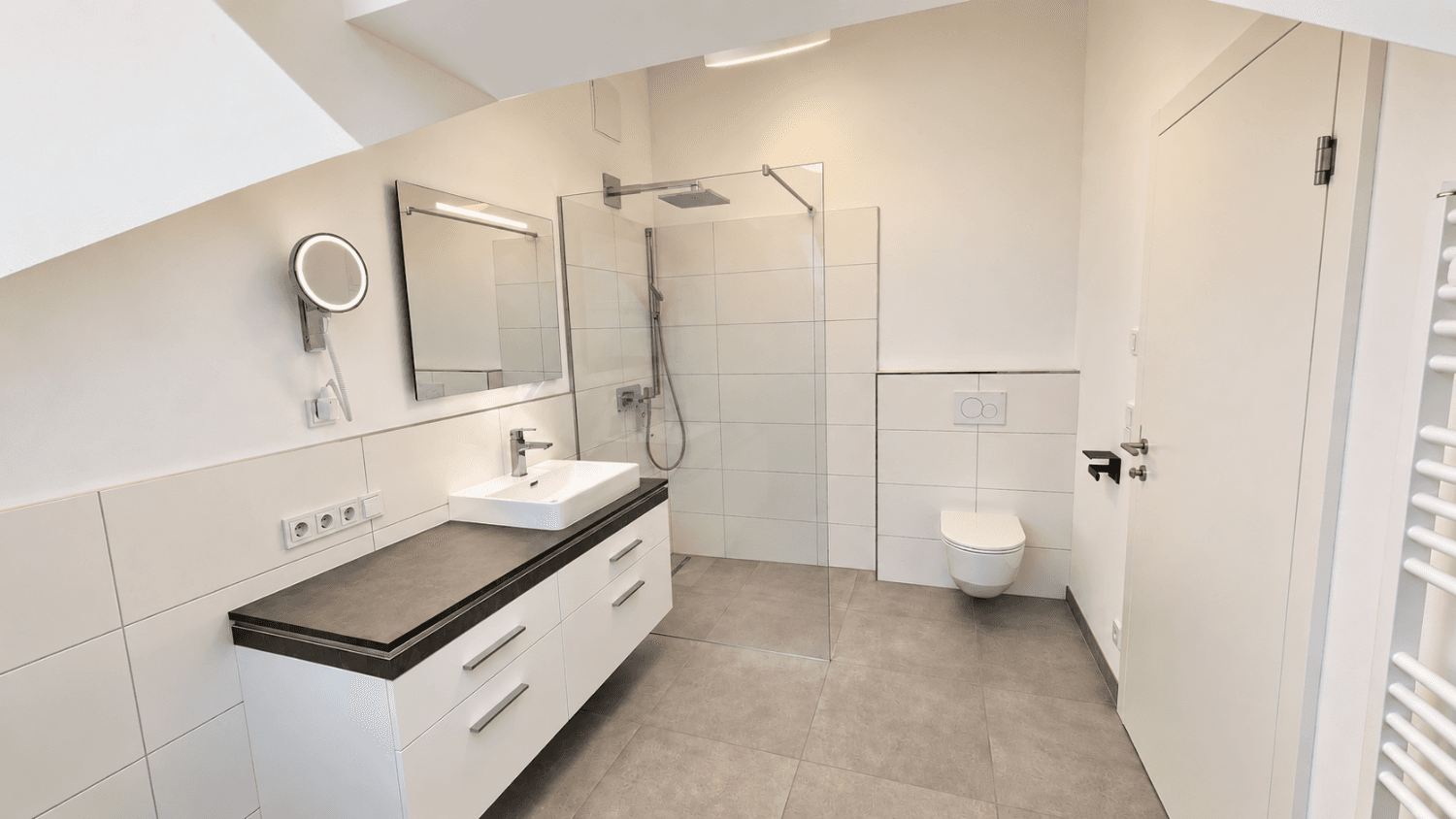 Modernes Badezimmer im Dachgeschoss mit Dusche, Waschbecken und wandhängendem WC.
