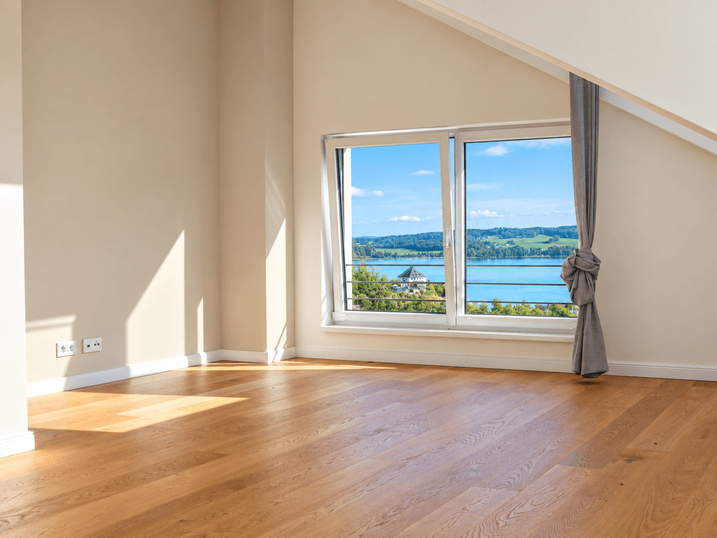 Helles Schlafzimmer im Dachgeschoss mit Holzboden und großem Fenster mit Seeblick.
