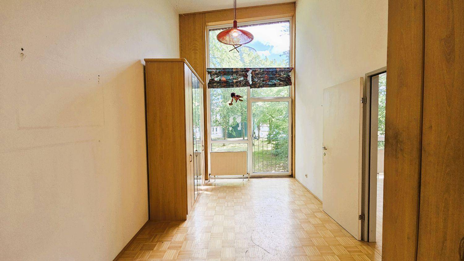 Leeres Zimmer mit Parkettboden, Holzverkleidung und hohen Fenstern zum Außenbereich.