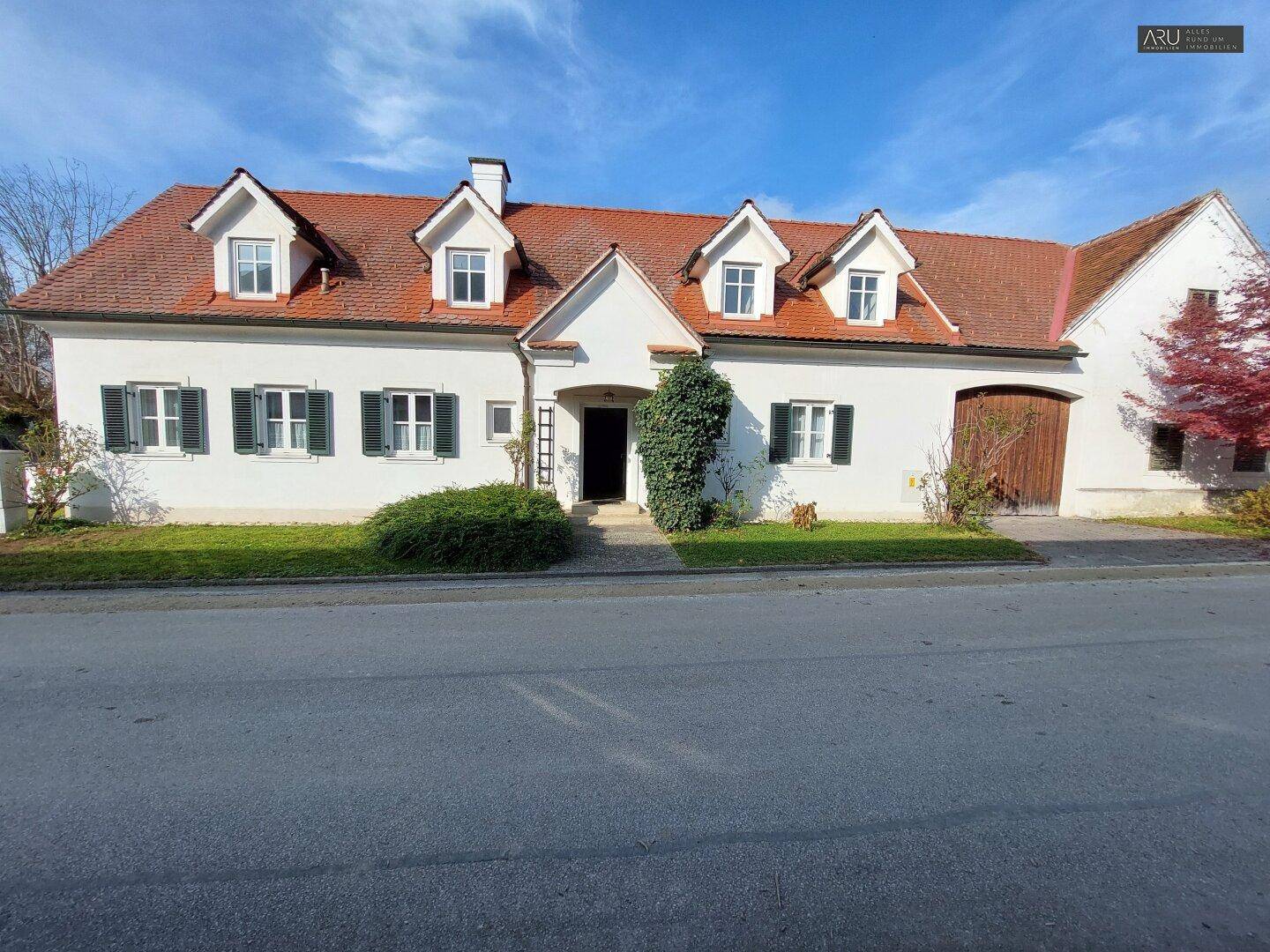 Charmantes Landhaus mit weißer Fassade, grünen Fensterläden und rotem Ziegeldach an einer ruhigen Straße.