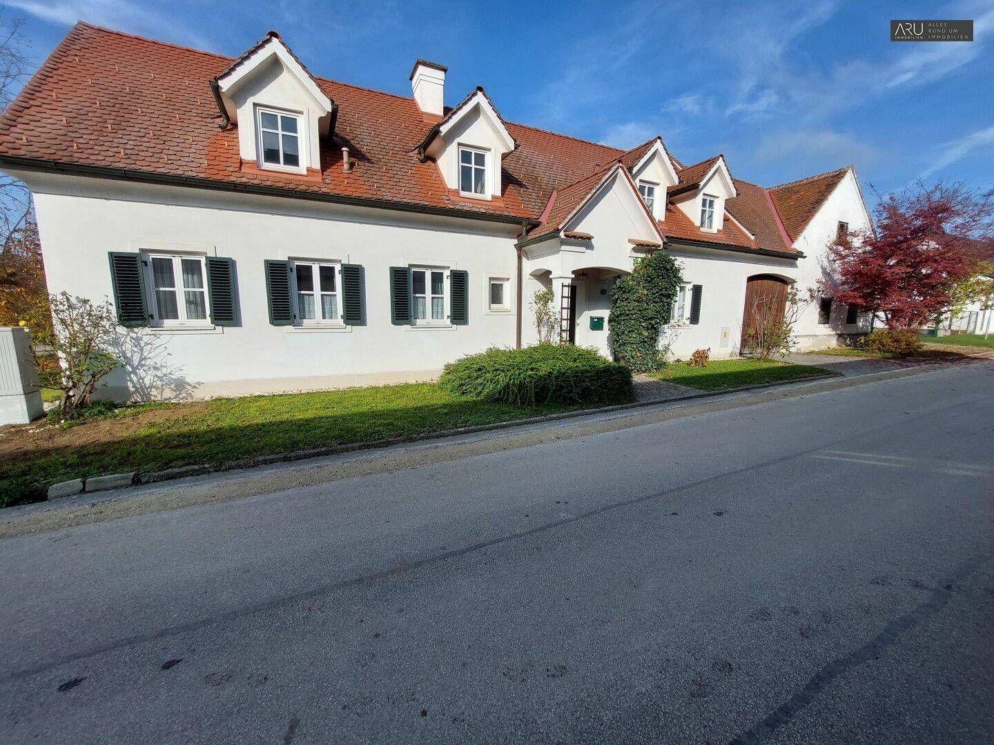 Frontansicht eines traditionellen Landhauses mit weißer Fassade, grünen Fensterläden und rotem Ziegeldach.