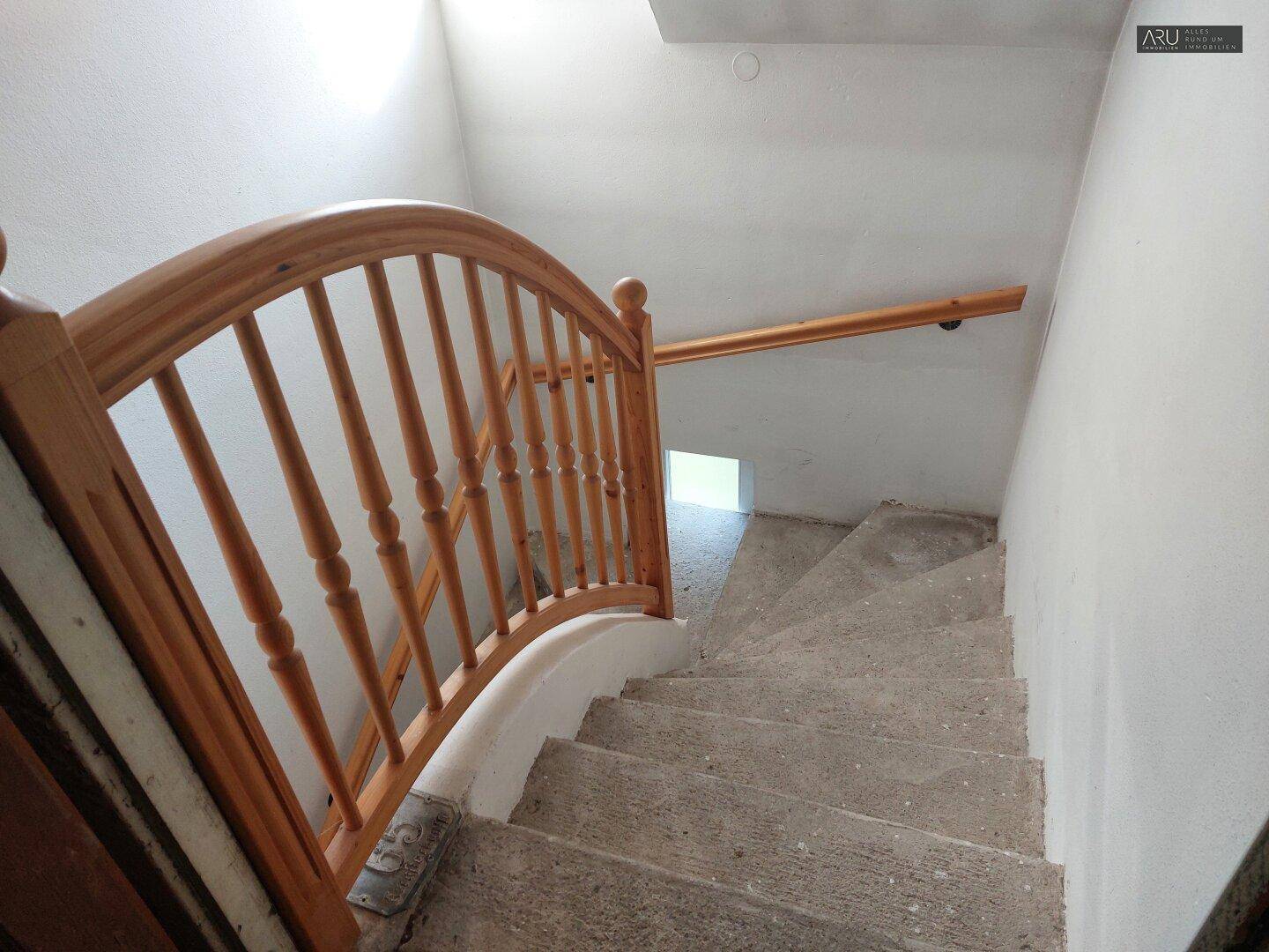 Steintreppe mit Holzgeländer, die in ein oberes Stockwerk führt.