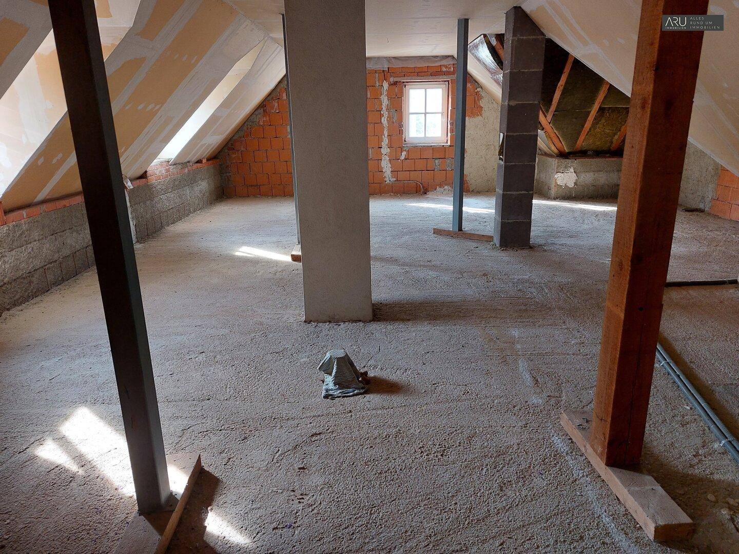 Unausgebauter Dachboden mit sichtbaren Dachschrägen, Ziegelwänden und Stützpfeilern.