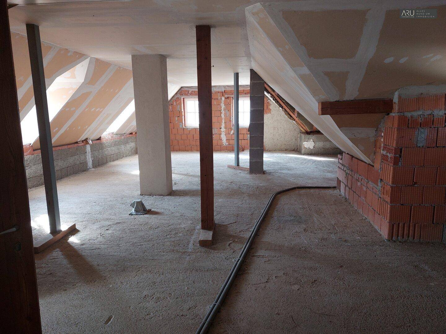 Geräumiger unausgebauter Dachboden mit Ziegelwänden, Stützpfeilern und Fenstern in den Dachschrägen.